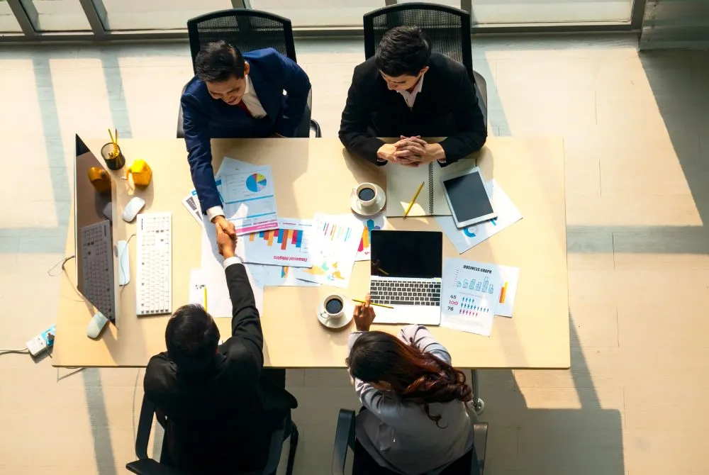 A group of professionals sitting around a table with papers and laptops, engaged in a business meeting.