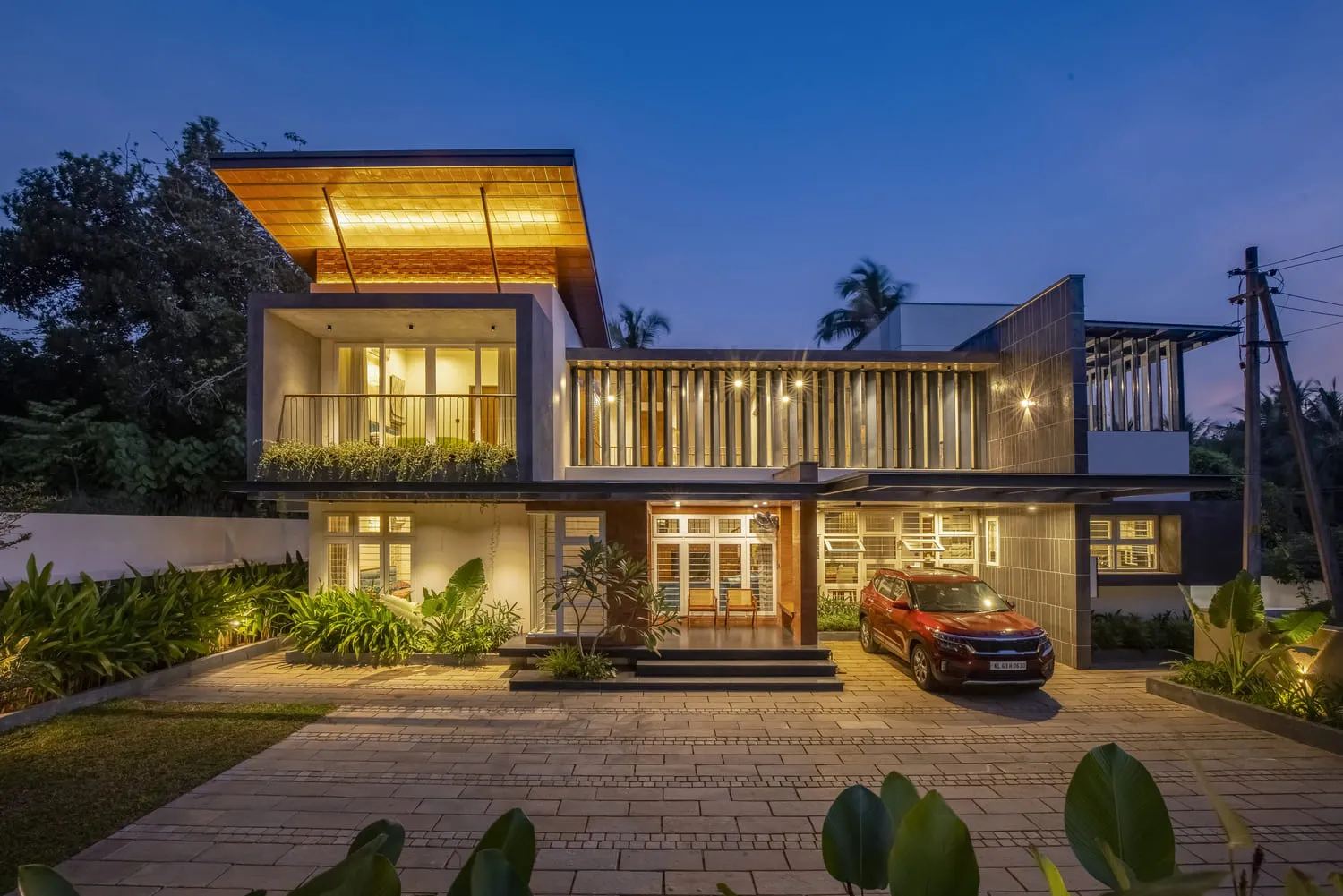 Modern two-story house with lit interior and exterior lights at dusk, featuring a car parked outside.