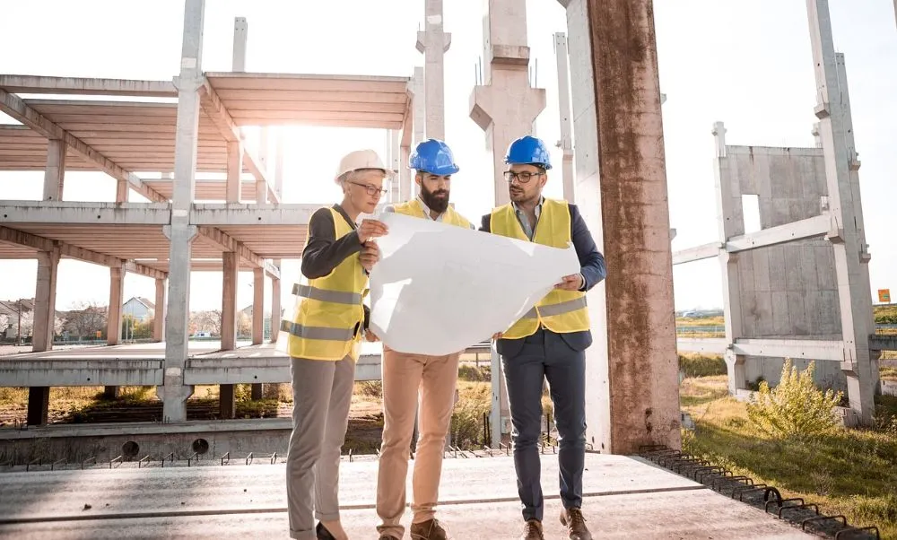  Three men in hard hats and safety vests standing in front of a building.