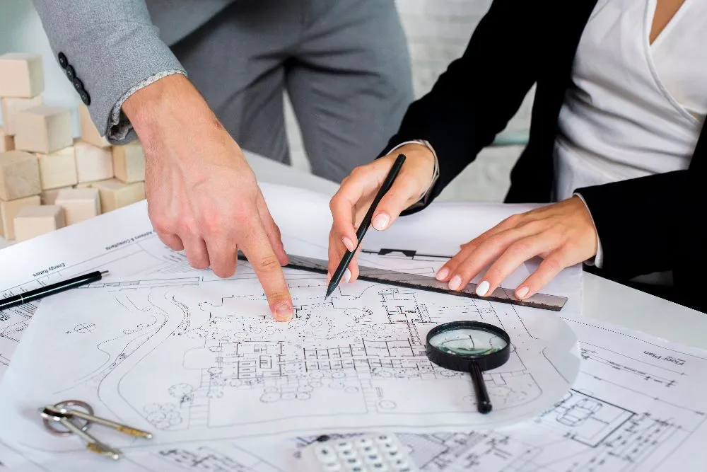 Two people intently examining a blueprint with a magnifying glass, focusing on every detail.